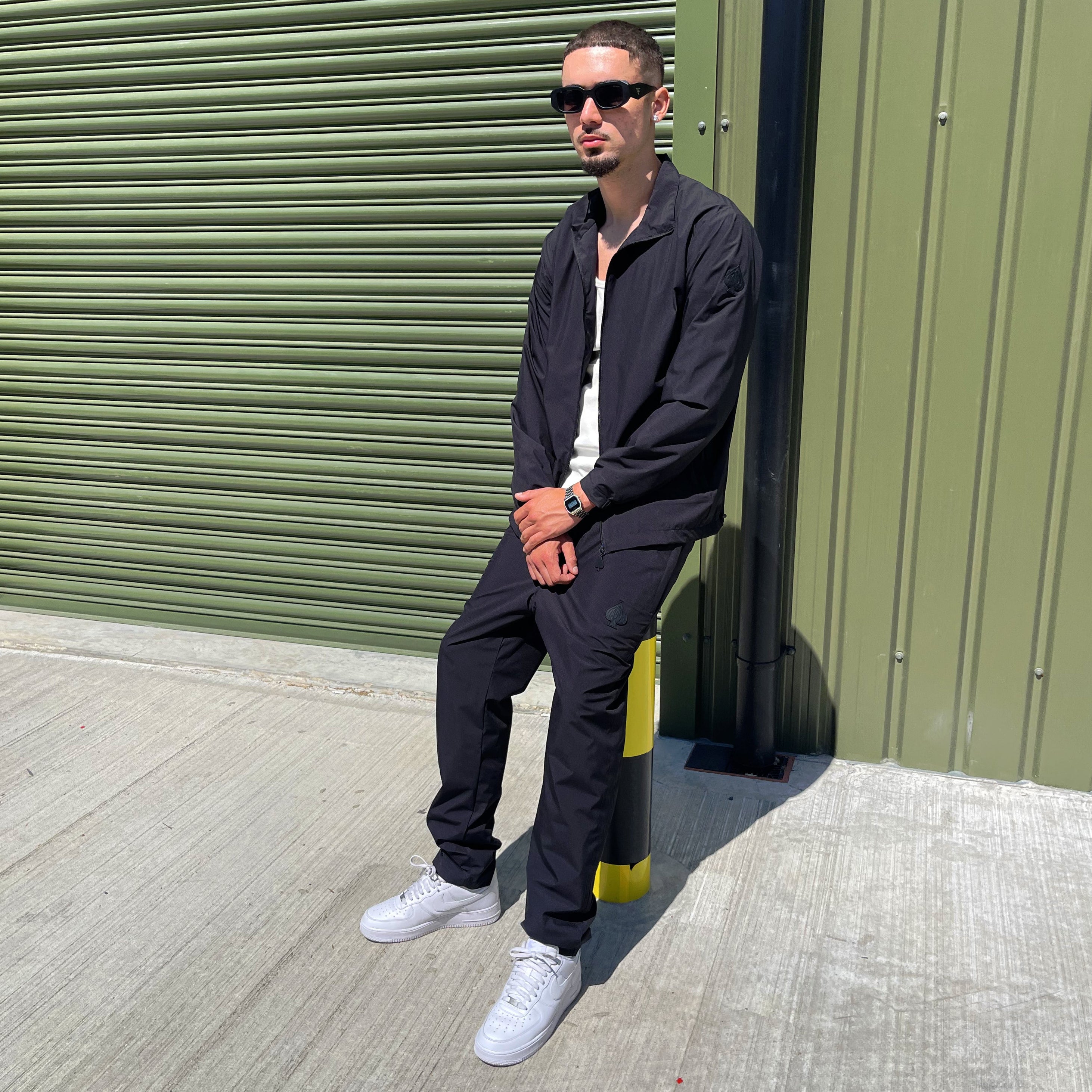 Sleek black streetwear set for men by Gabos London, shot in an industrial setting to highlight the bold simplicity of the outfit. Windbreaker 