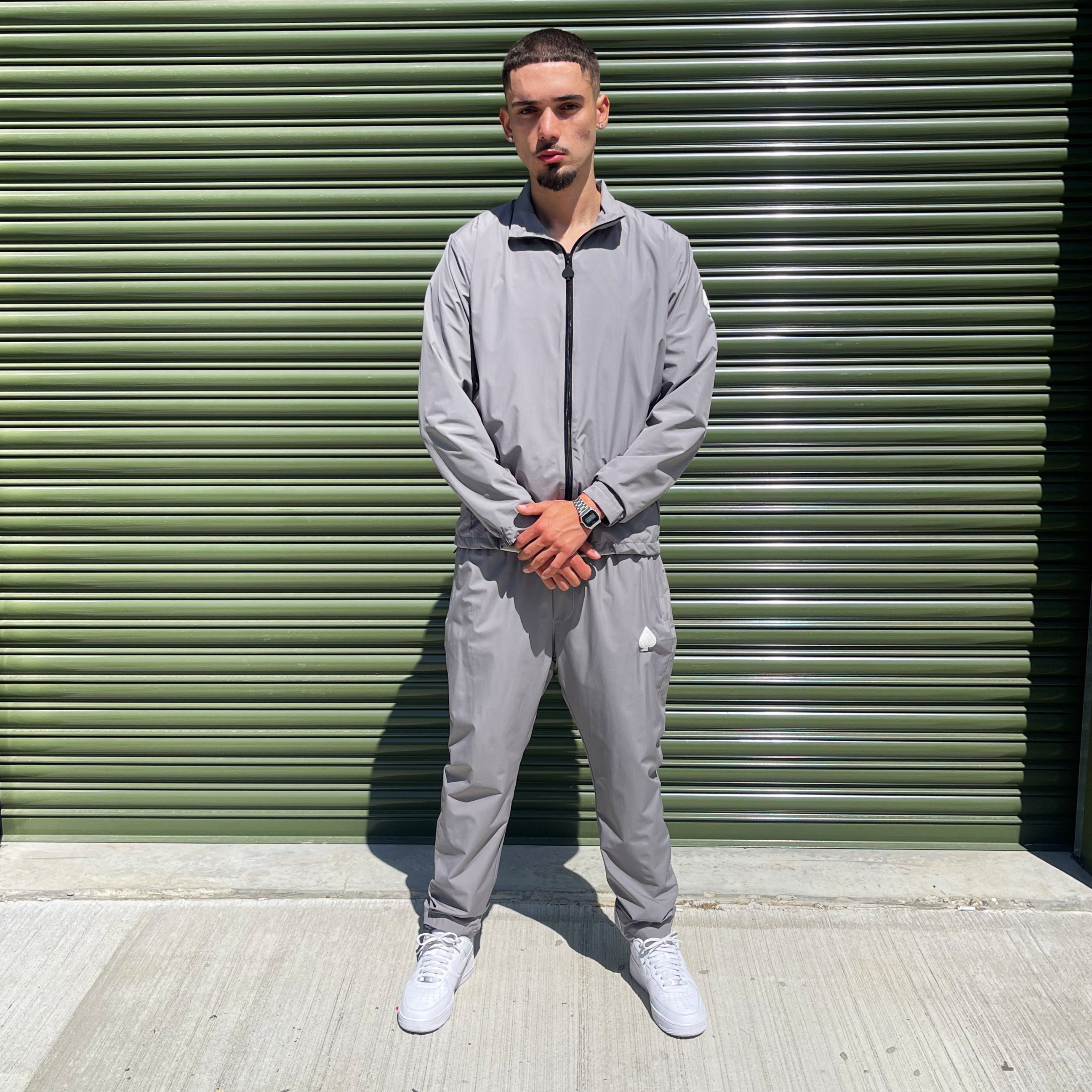 Gabos London grey 3-piece tracksuit set with matching trousers, worn by male model in urban industrial setting – streetwear for SS25