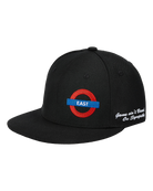 A black flat-brim baseball cap featuring an embroidered red and blue London Underground roundel with the word 'EAST' on the front, and white script embroidery on the side.